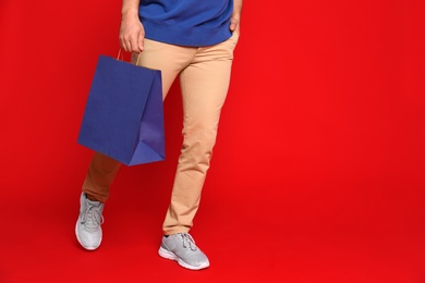 Young man with paper bag on red background, closeup. Space for text