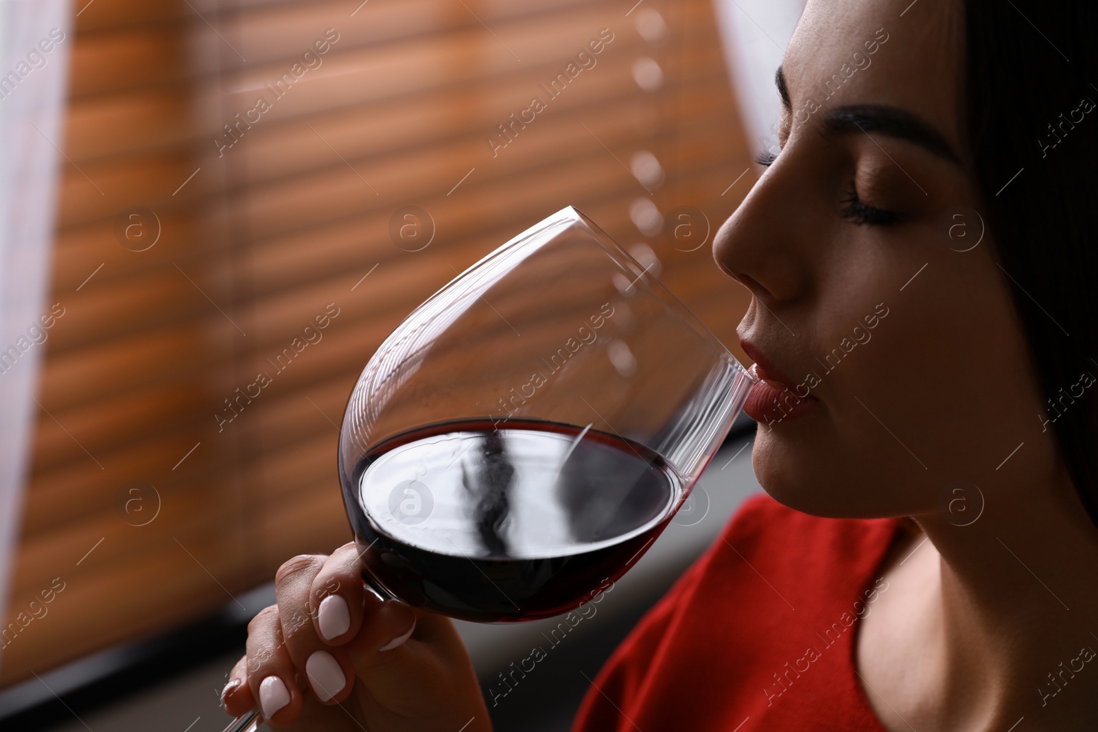 Photo of Beautiful young woman with glass of luxury red wine indoors, closeup view. Space for text