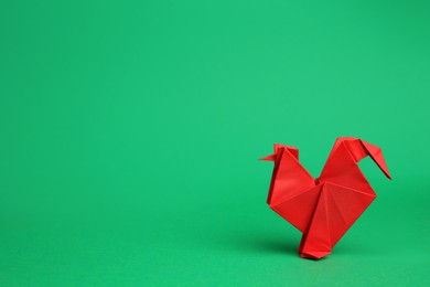 Origami art. Handmade red paper rooster on green background, space for text