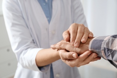 Female doctor comforting man on light background, closeup of hands. Help and support concept