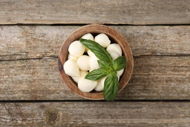 Photo of Tasty mozzarella balls and basil leaves in bowl on wooden table, top view