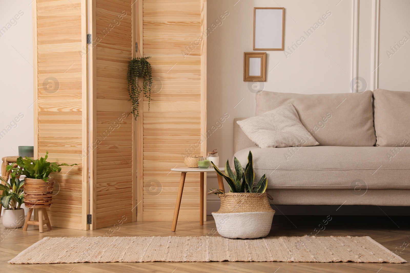 Photo of Stylish room with wooden folding screen and comfortable sofa near white wall. Interior design