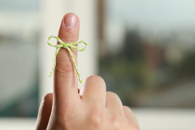 Man showing index finger with tied bow as reminder on blurred background, closeup