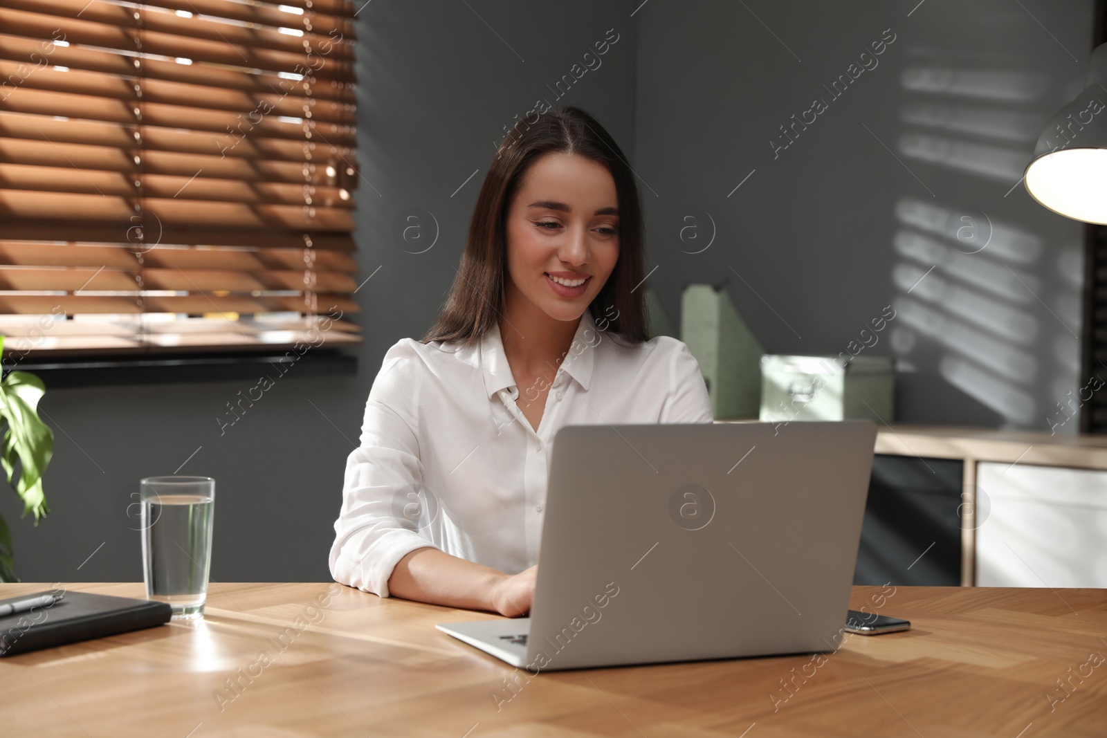 Photo of Young woman using laptop for search at wooden table in office