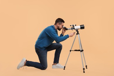 Photo of Astronomer looking at stars through telescope on beige background