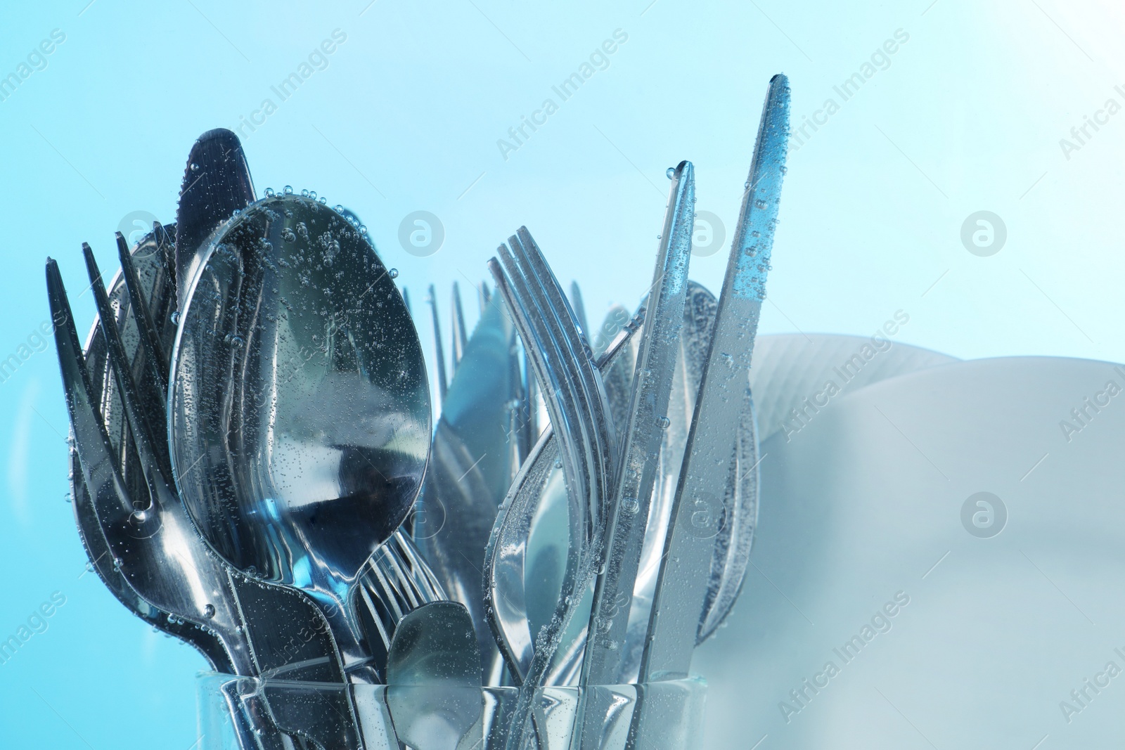 Photo of Washing silver cutlery and plates in water on light blue background