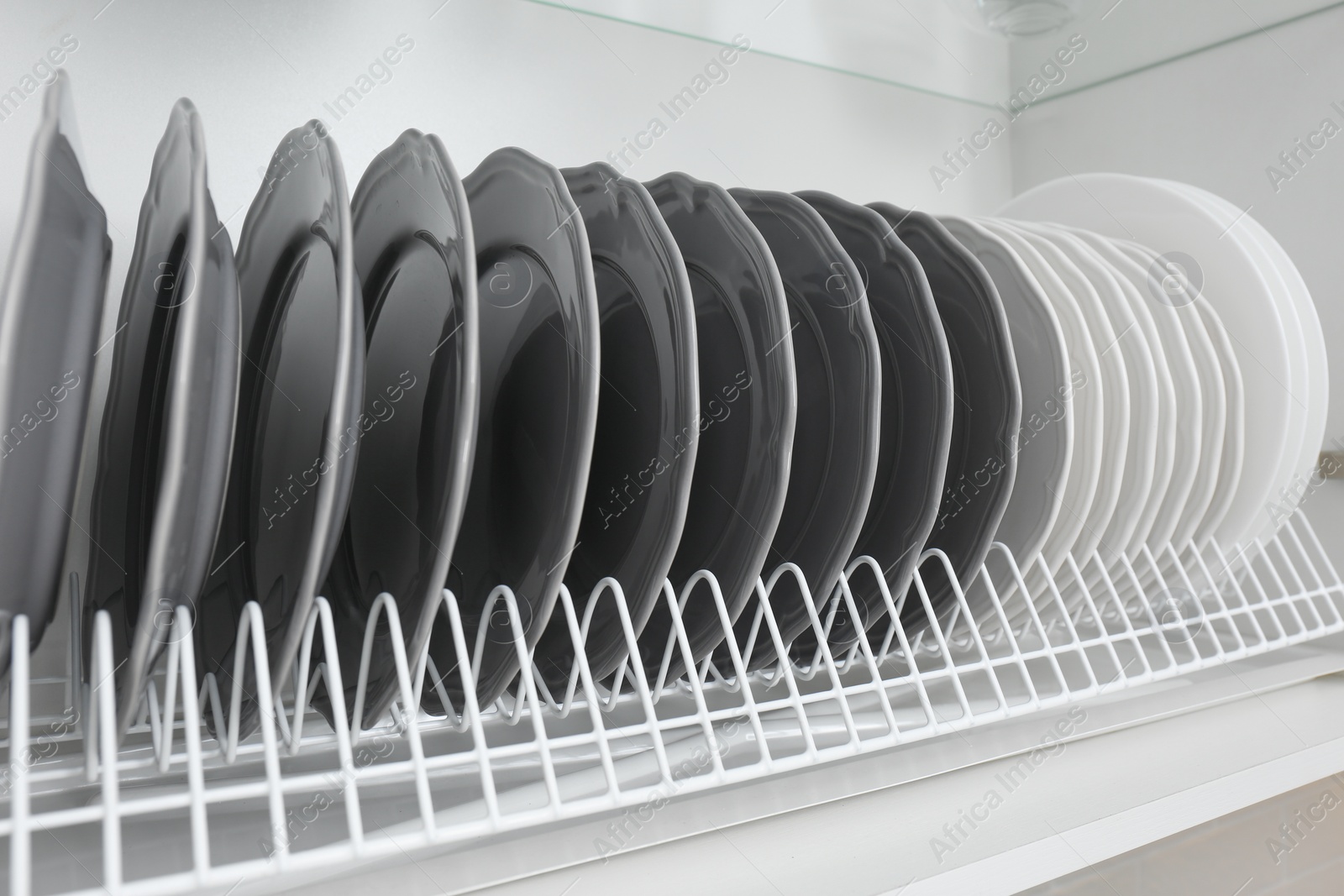 Photo of Drying rack with clean plates in kitchen cabinet, closeup
