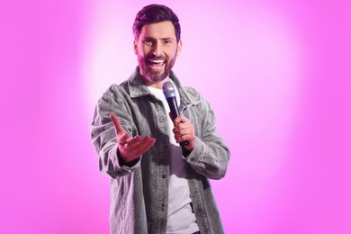 Photo of Handsome man with microphone singing on pink background