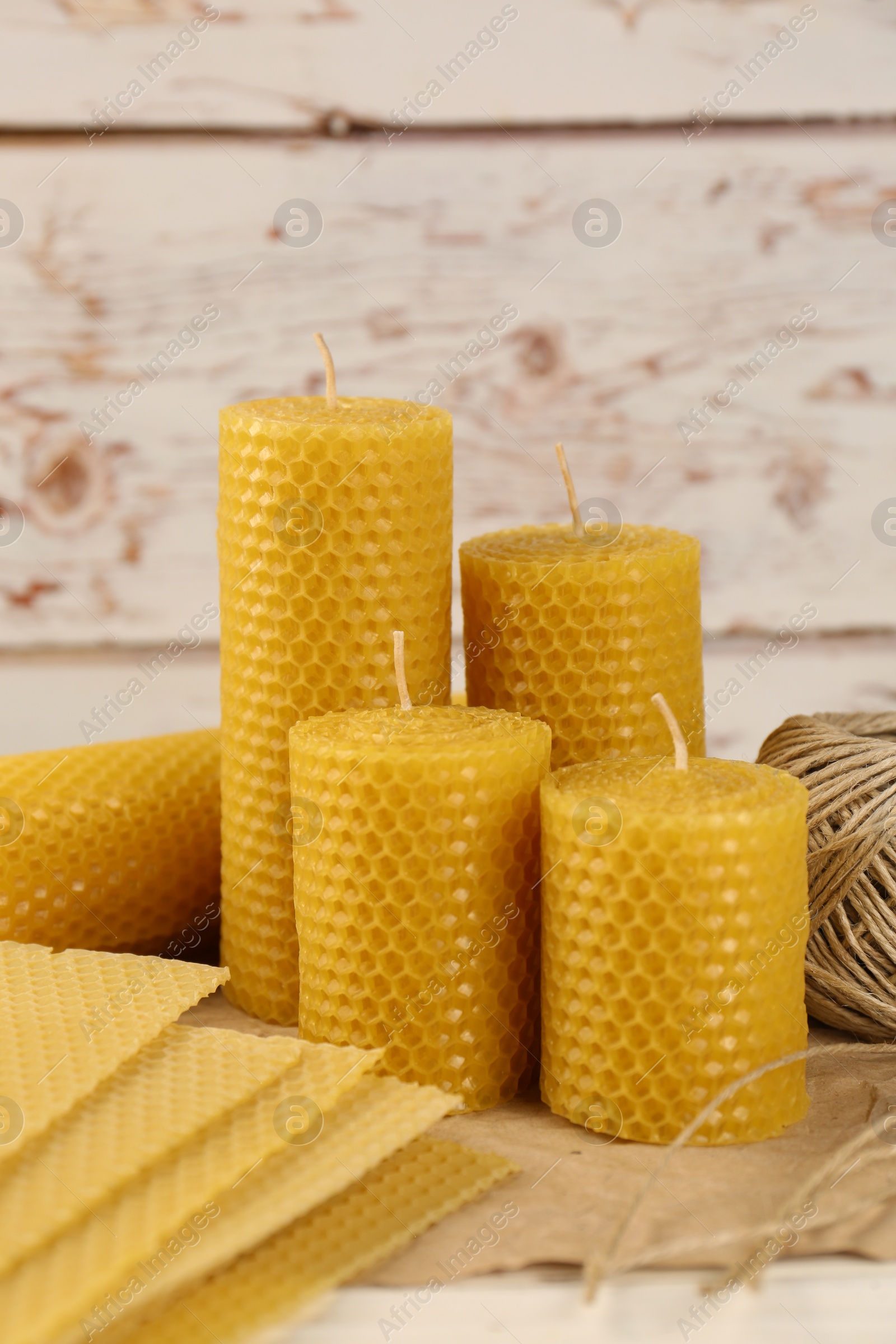Photo of Stylish elegant beeswax candles, wax sheets and jute twine on white wooden table