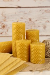 Stylish elegant beeswax candles, wax sheets and jute twine on white wooden table