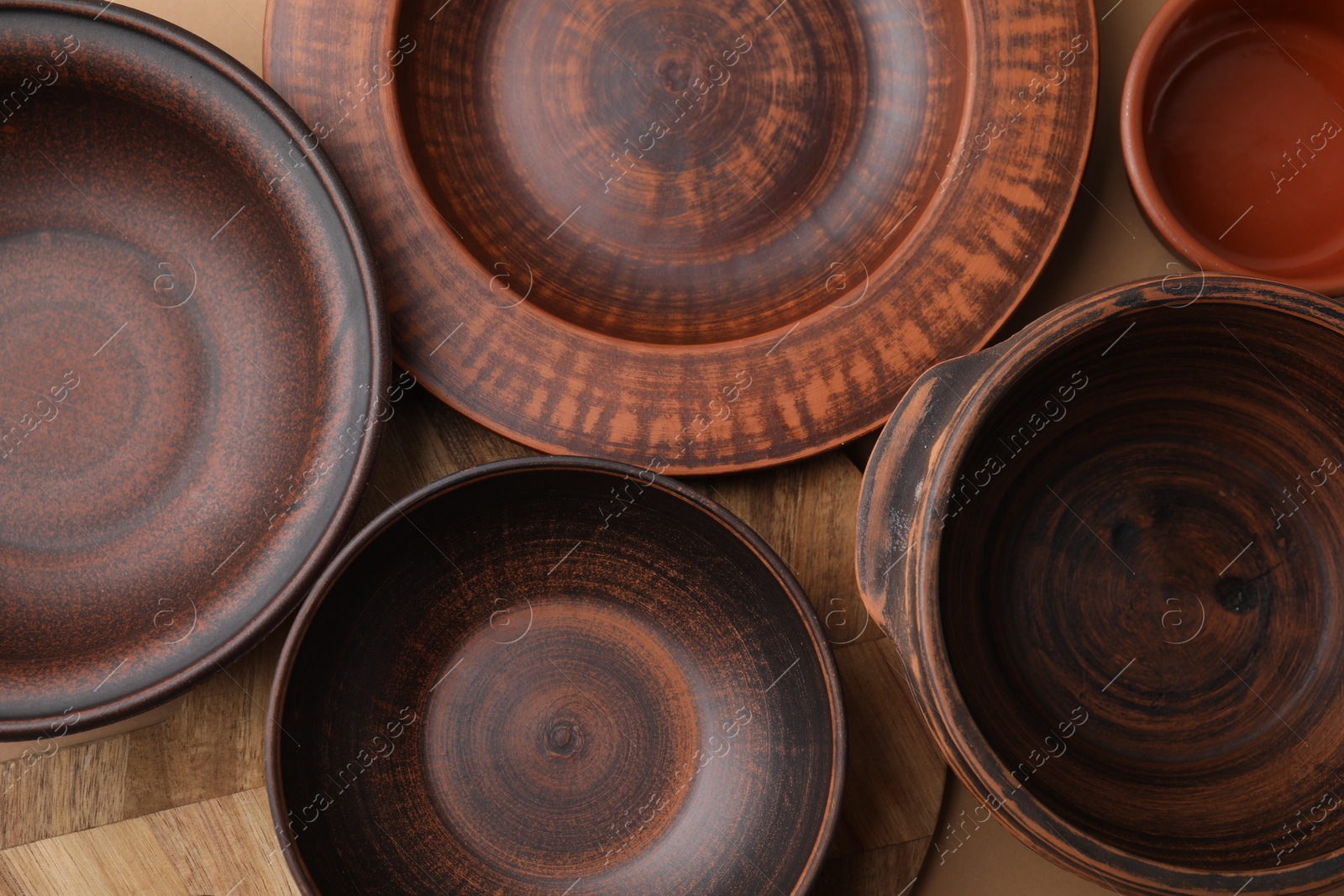 Photo of Ceramic bowls, wooden board and plate on beige background, flat lay