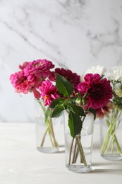 Bouquet of beautiful wild flowers and leaves in vases on white wooden table against marble background