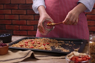 Woman putting granola from baking tray into jar at table, closeup