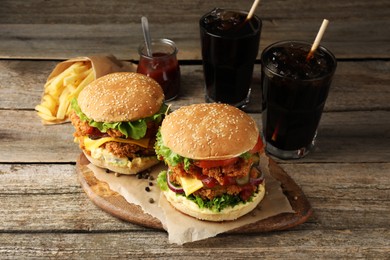 Photo of Delicious burgers with crispy chicken patty, french fries and soda drinks on wooden table