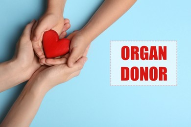 Image of Organ donor. Woman and child holding heart on light blue background, top view