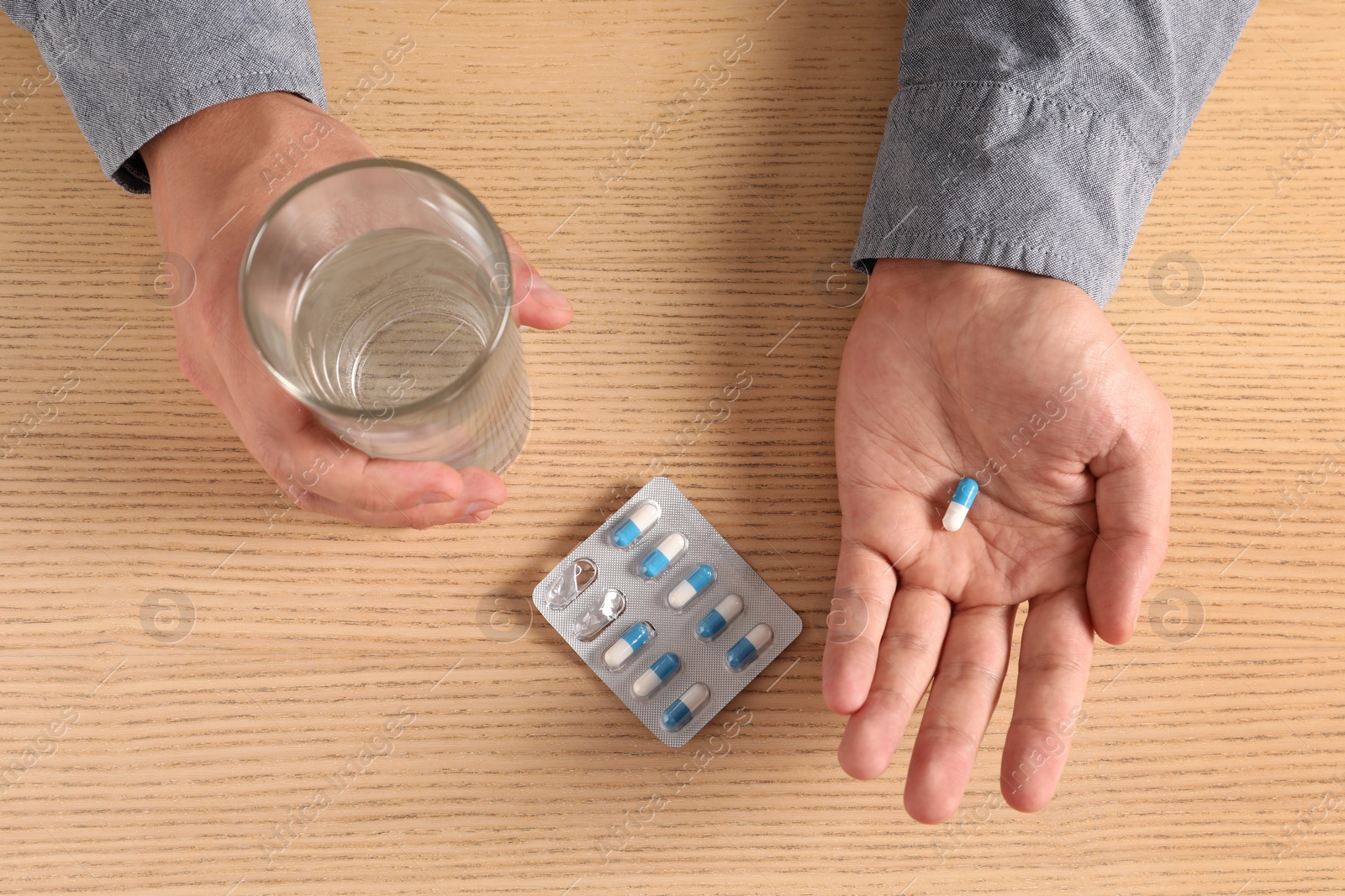 Photo of Man with glass of water and pill at wooden table, top view