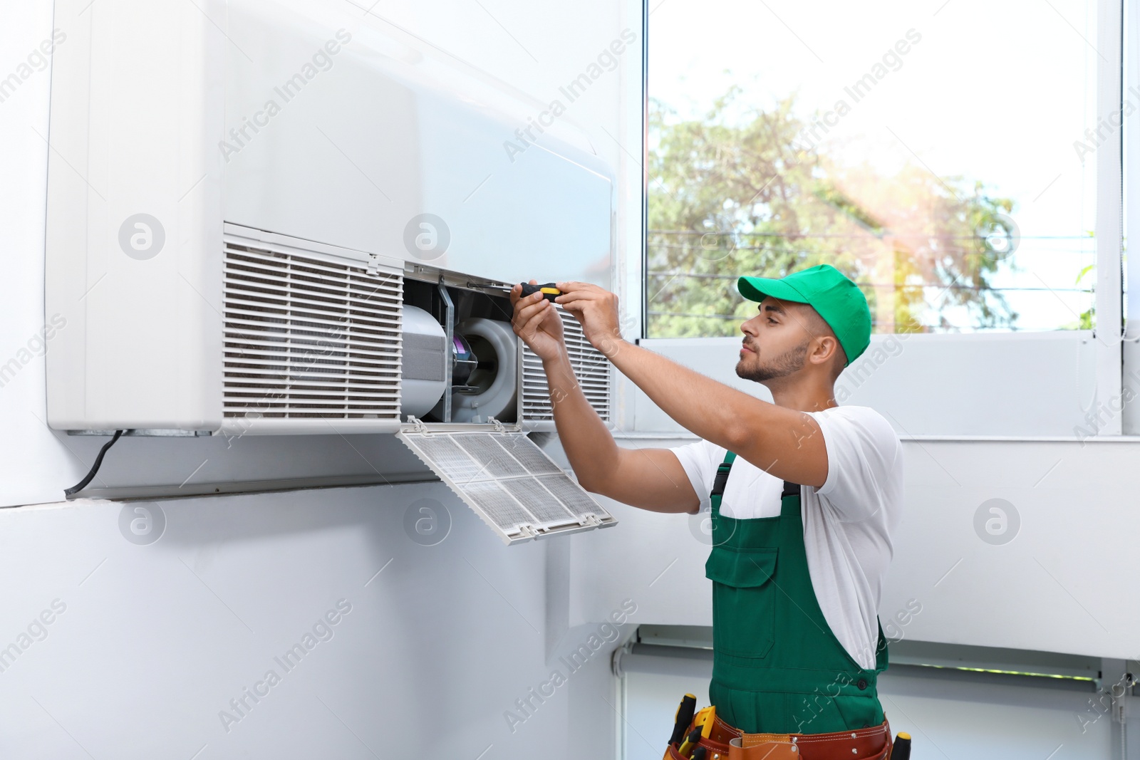 Photo of Professional technician maintaining modern air conditioner indoors