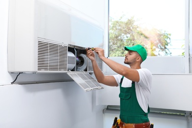 Photo of Professional technician maintaining modern air conditioner indoors