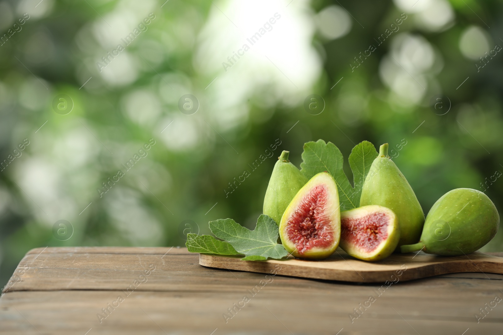 Photo of Cut and whole green figs on wooden table against blurred background, space for text