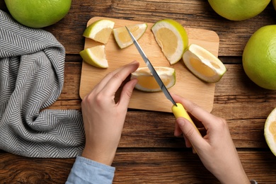 Woman cutting sweetie fruit at wooden table, top view