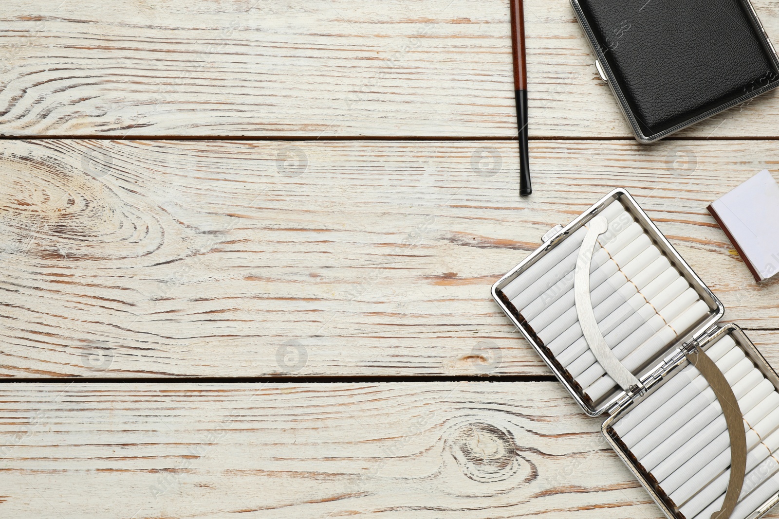 Photo of Cigarettes, holder, cases and matchbox on white wooden table, flat lay. Space for text