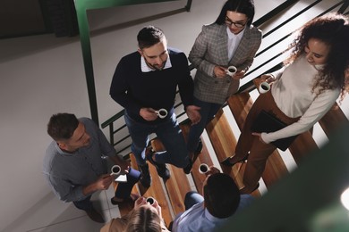 Photo of Group of coworkers talking during coffee break on stairs in office, above view
