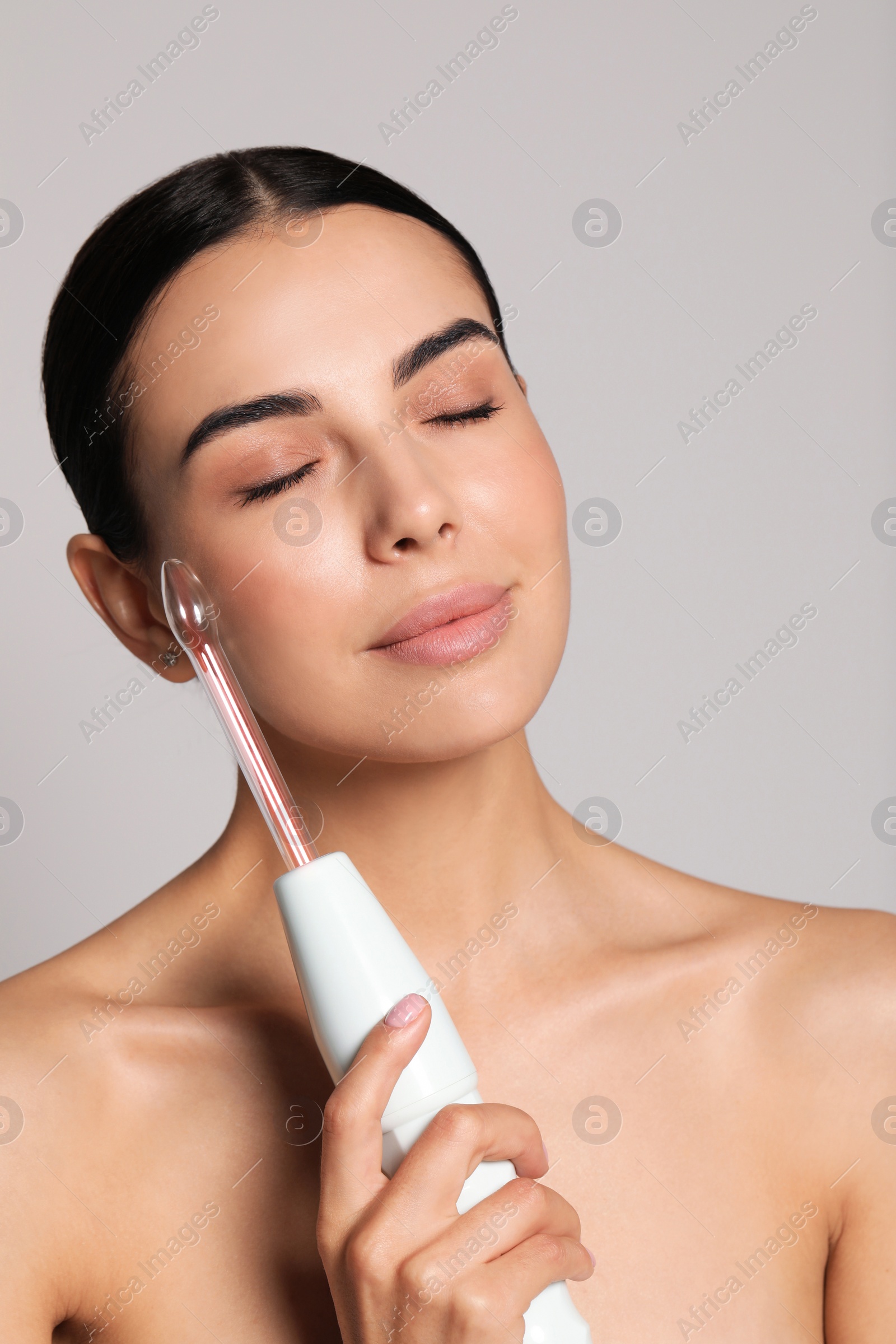 Photo of Woman using high frequency darsonval device on grey background