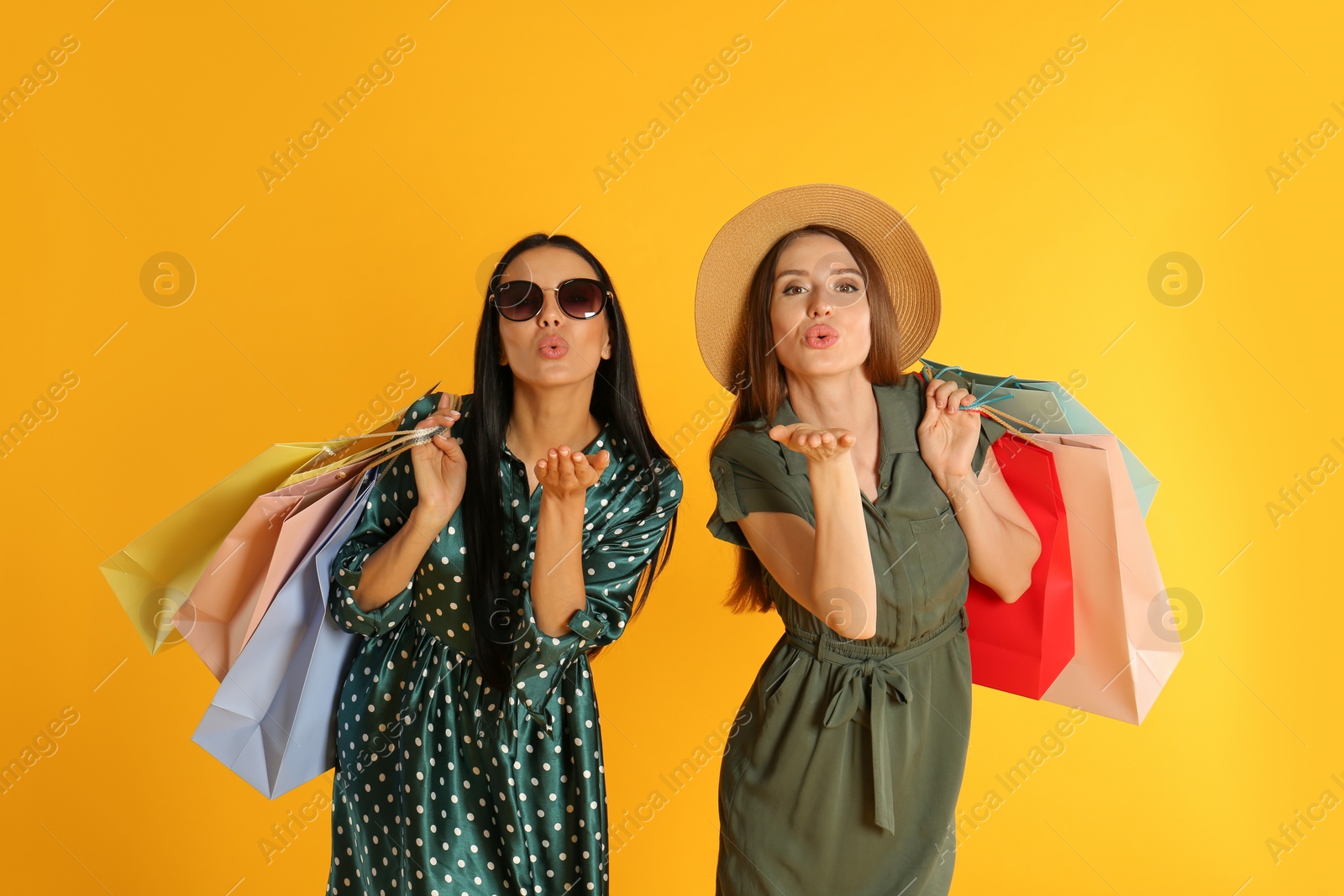 Photo of Beautiful young women with paper shopping bags on yellow background