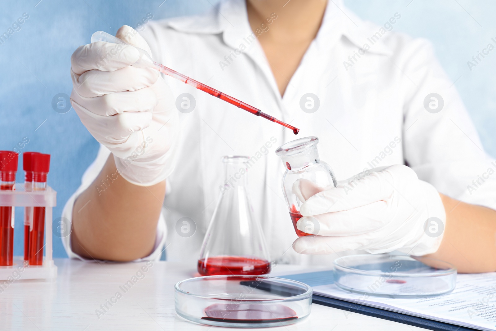 Photo of Scientist dripping blood into glass bottle at table, closeup. Virus research