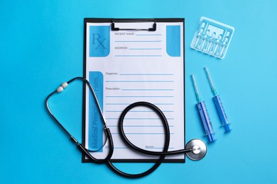 Photo of Clipboard with medical prescription form, stethoscope, ampoules and syringes on light blue background, flat lay
