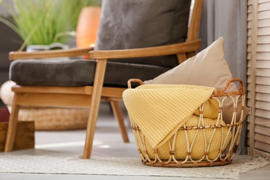 Basket with soft plaid and pillows near armchair in room