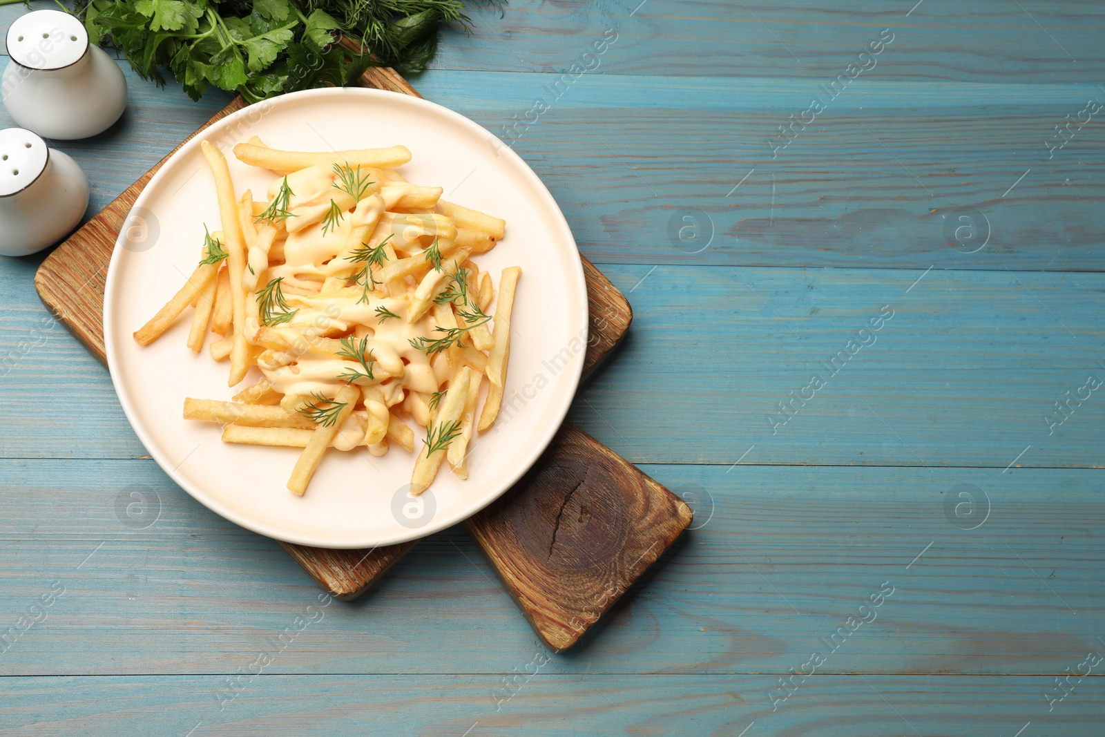 Photo of Delicious french fries with cheese sauce and dill on light blue wooden table, flat lay. Space for text