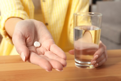 Woman with pill and glass of water at table, closeup