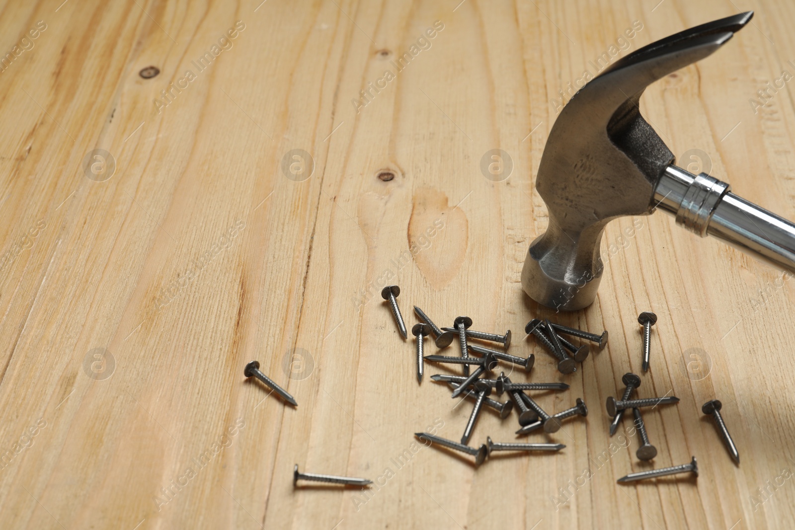 Photo of New hammer and metal nails on wooden table. Space for text