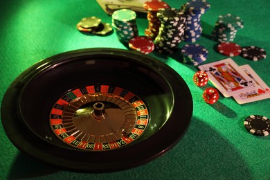 Photo of Roulette wheel with ball, playing cards and chips on green table. Casino game