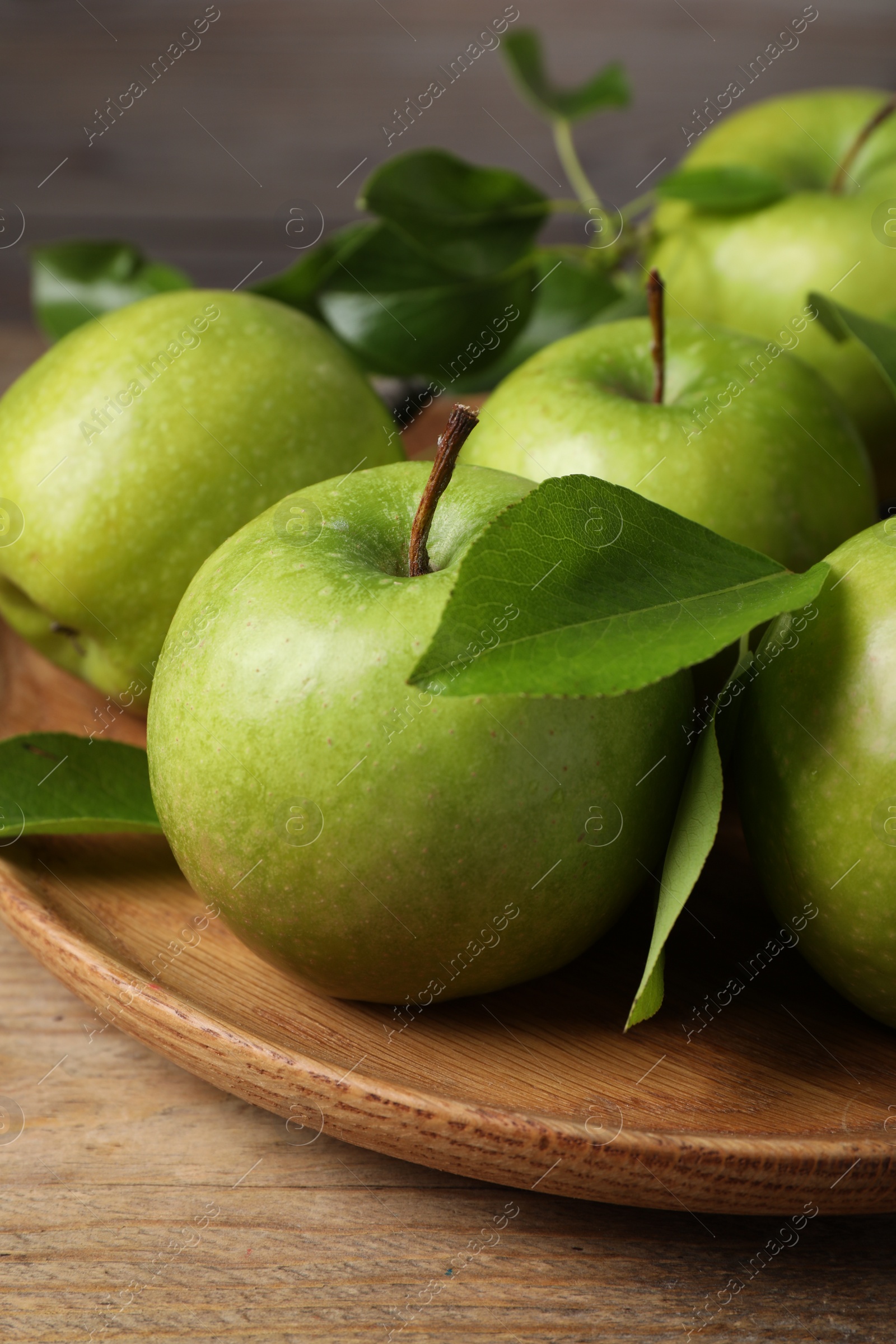 Photo of Fresh ripe green apples and leaves on wooden plate, closeup
