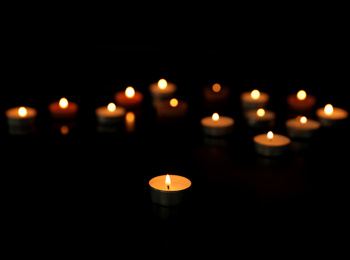 Photo of Many burning tealight candles on dark background