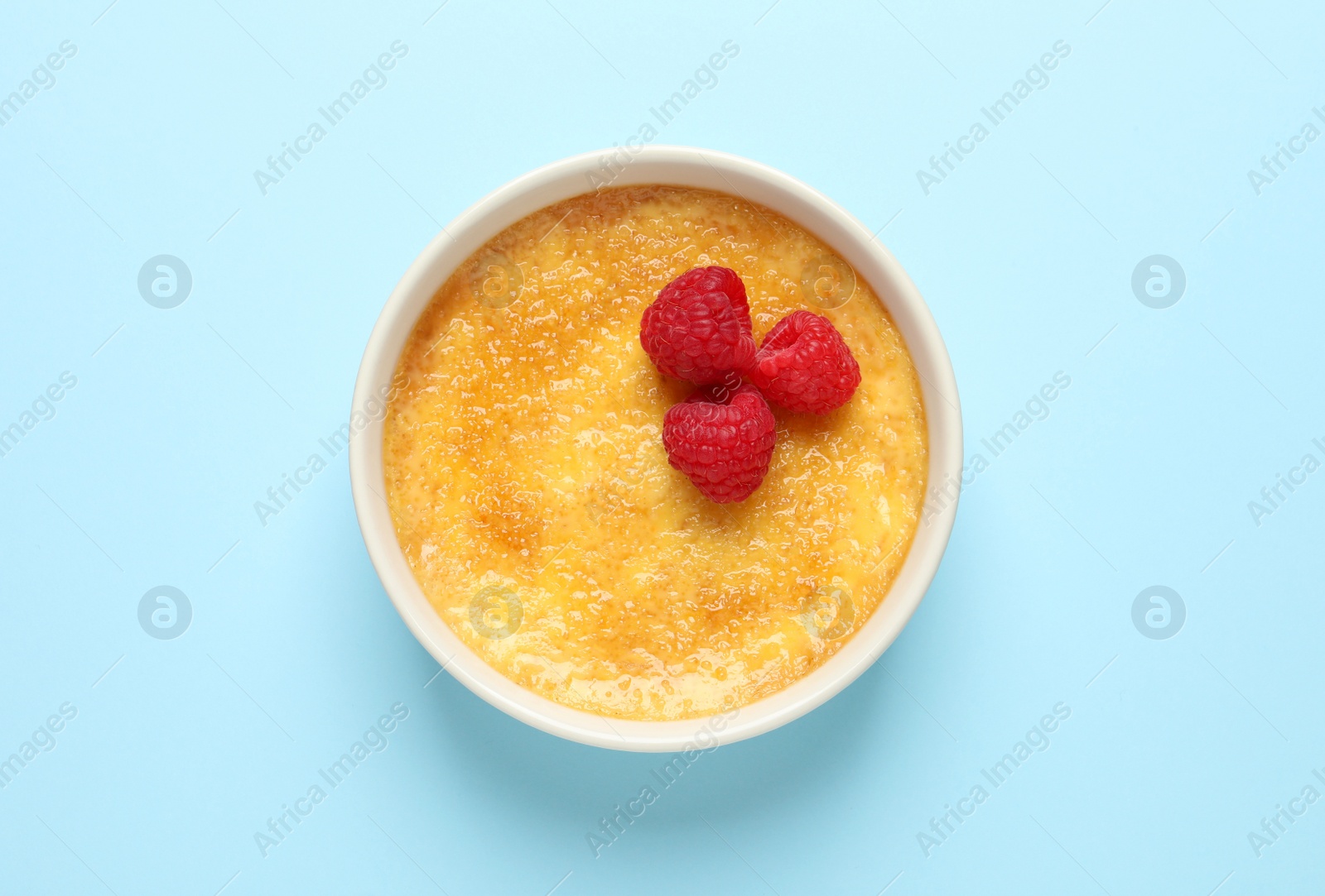 Photo of Delicious creme brulee with fresh raspberries on light blue background, top view
