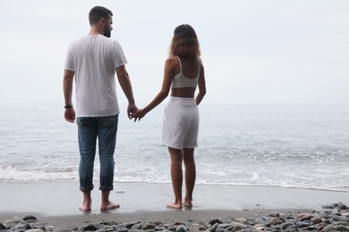 Photo of Young couple on sandy beach near sea, back view