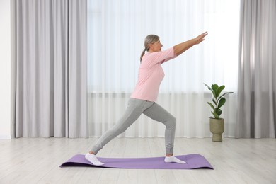 Photo of Senior woman practicing yoga on mat at home