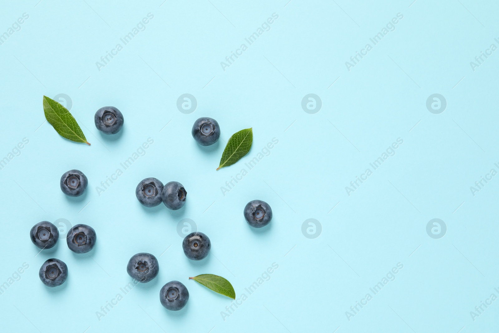 Photo of Tasty fresh blueberries with green leaves on light blue background, flat lay. Space for text