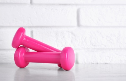 Photo of Stylish dumbbells on table against brick wall, space for text. Home fitness