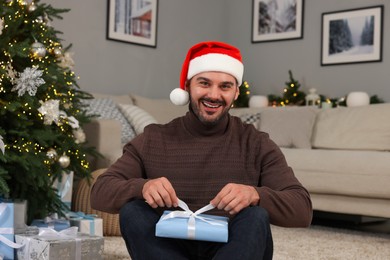 Happy man in Santa hat opening Christmas gift at home