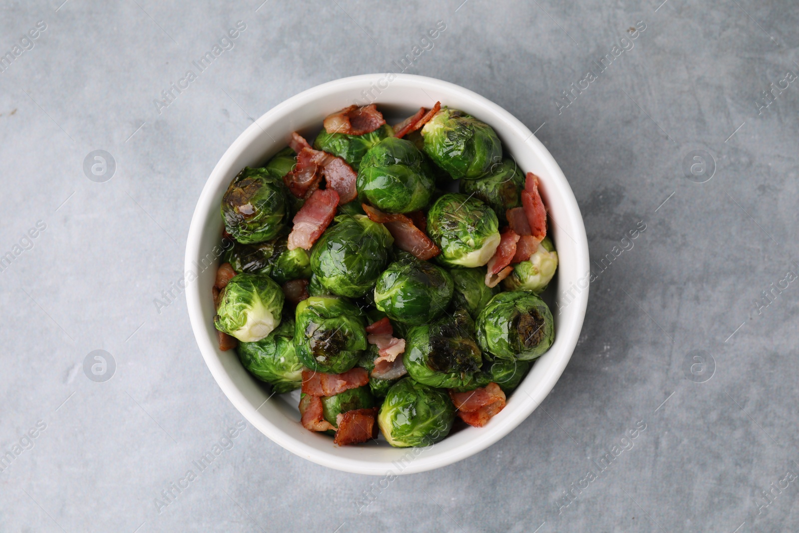 Photo of Delicious roasted Brussels sprouts and bacon in bowl on grey table, top view