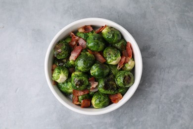 Delicious roasted Brussels sprouts and bacon in bowl on grey table, top view