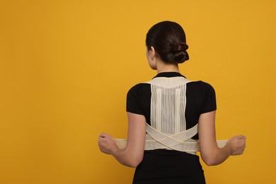 Woman with orthopedic corset on orange background, back view. Space for text