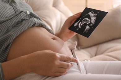 Photo of Pregnant young woman holding ultrasound picture near her belly at home, closeup