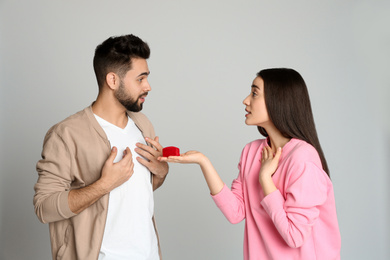Photo of Young woman with engagement ring making marriage proposal to her boyfriend on light grey background