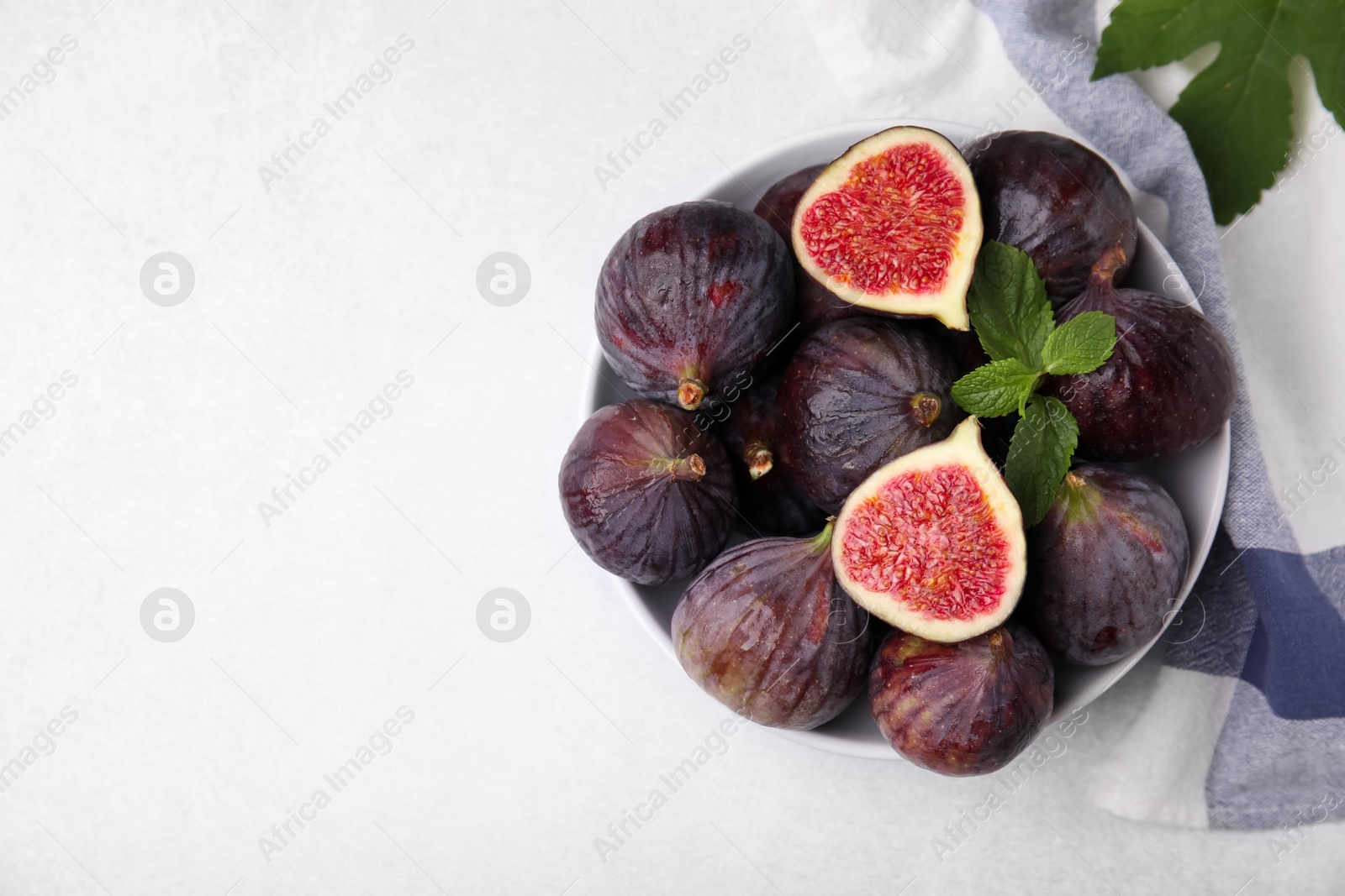 Photo of Bowl of tasty ripe figs on light table, top view. Space for text