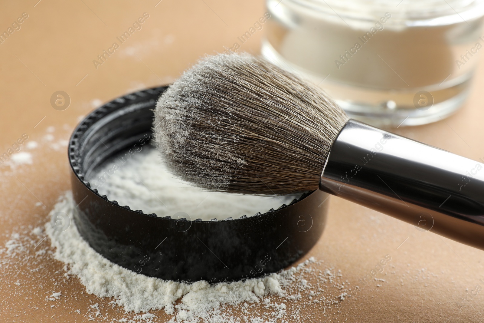 Photo of Makeup brush and lid with rice loose face powder on brown background, closeup